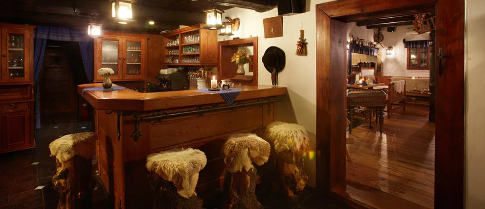 Dřevěný bar koliby s barovými stoličkami pokrytými ovčími kožešinami